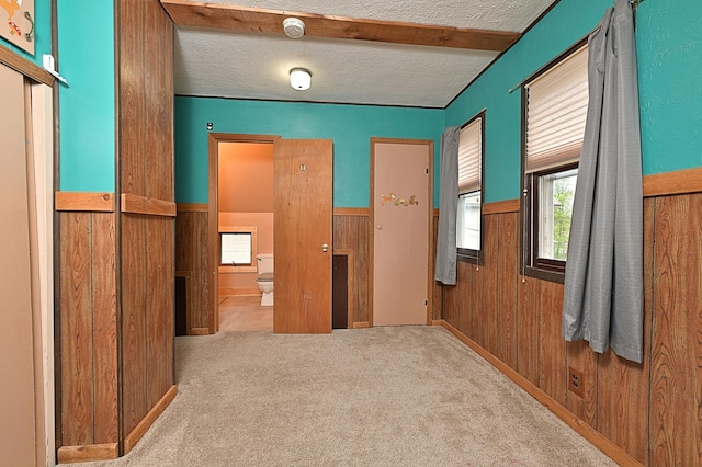 hall featuring wood walls, carpet, a textured ceiling, and wainscoting