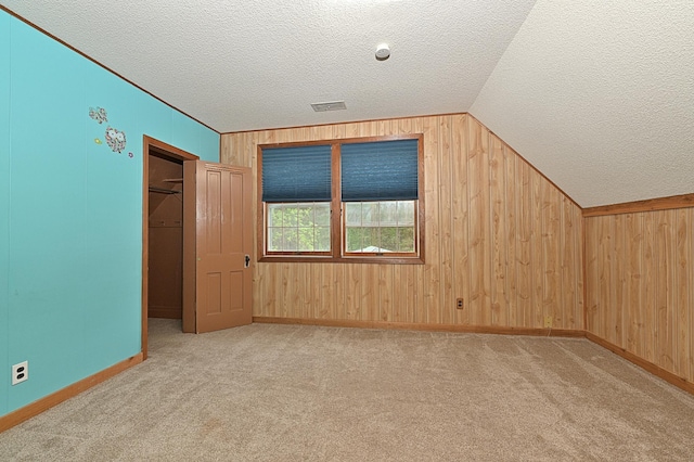 bonus room with a textured ceiling, wooden walls, lofted ceiling, carpet flooring, and baseboards