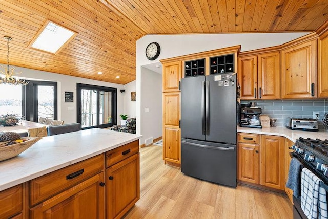 kitchen with wood ceiling, black gas range oven, lofted ceiling with skylight, freestanding refrigerator, and a chandelier