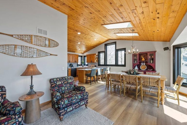 dining area with lofted ceiling with skylight, a healthy amount of sunlight, light wood finished floors, visible vents, and a chandelier