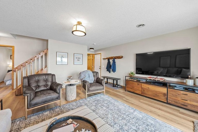 living area featuring stairway, visible vents, a textured ceiling, and wood finished floors