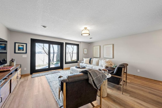 living room with light wood-style floors, visible vents, baseboards, and a textured ceiling