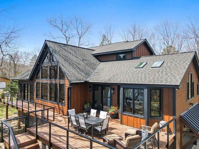 back of property featuring roof with shingles, outdoor dining space, and a wooden deck