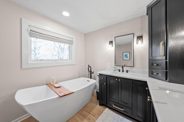 full bathroom with vanity, a soaking tub, and wood finished floors