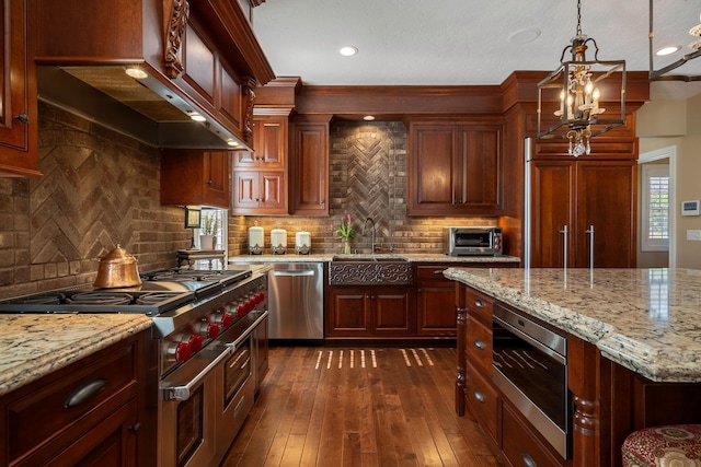 2834 12th Ave NW, Austin, MN 55912 - kitchen featuring stainless steel appliances, a sink, wall chimney range hood, light stone countertops, and decorative light fixtures