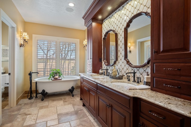 2834 12th Ave NW, Austin, MN 55912 - full bathroom with baseboards, toilet, a freestanding bath, double vanity, and stone finish flooring