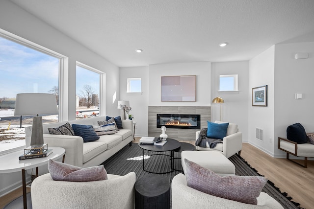 living room with a glass covered fireplace, baseboards, recessed lighting, visible vents, and light wood finished floors