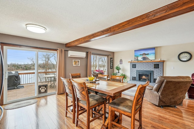 dining area with a wall unit AC, beam ceiling, a fireplace, a textured ceiling, and light wood-style floors
