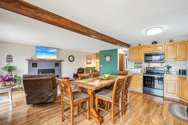 dining room featuring a fireplace, light wood finished floors, and beamed ceiling