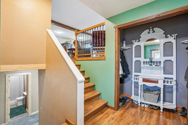 stairway featuring a textured wall, baseboards, and wood finished floors