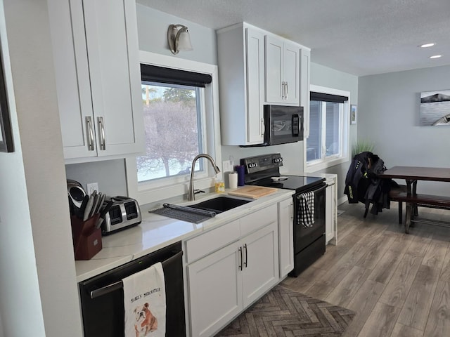 kitchen with a sink, white cabinets, black appliances, and light countertops