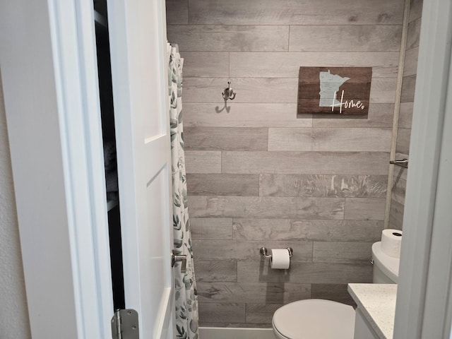 bathroom featuring vanity, a shower with shower curtain, wooden walls, and toilet