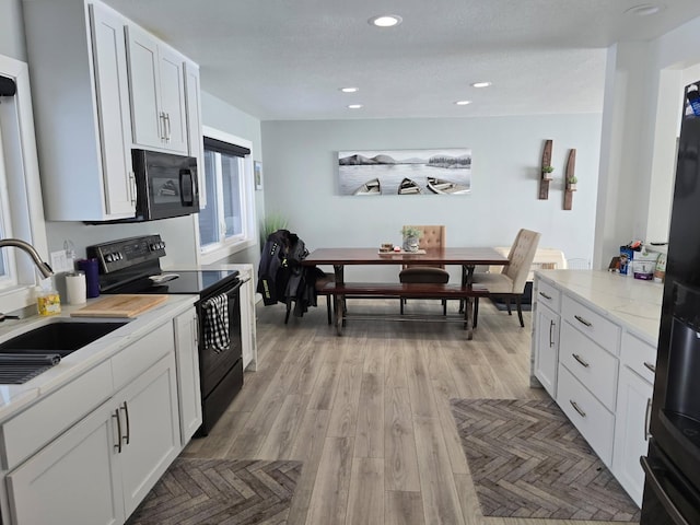 kitchen featuring light stone counters, a sink, white cabinetry, recessed lighting, and black appliances
