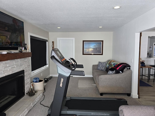 workout area with a fireplace with raised hearth, a textured ceiling, recessed lighting, and baseboards