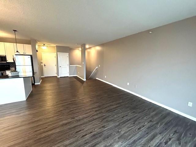 unfurnished living room featuring dark wood-style floors, baseboards, and a textured ceiling
