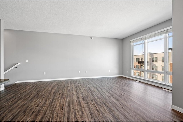 unfurnished living room with dark wood-style flooring, baseboards, and a textured ceiling