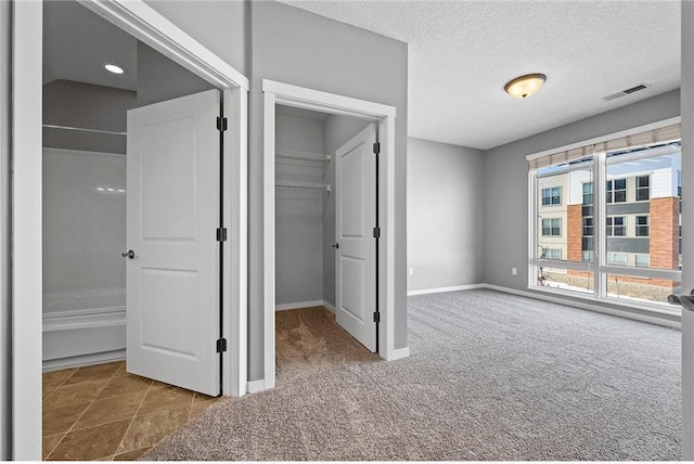 unfurnished bedroom featuring baseboards, carpet flooring, a textured ceiling, a walk in closet, and visible vents