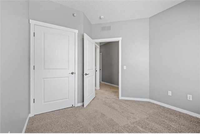 unfurnished bedroom with a textured ceiling, light colored carpet, baseboards, and visible vents