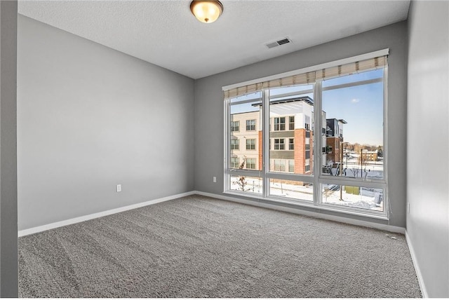 spare room with a textured ceiling, baseboards, visible vents, and carpet floors
