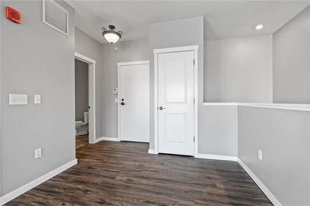 empty room featuring visible vents, baseboards, a textured ceiling, and wood finished floors