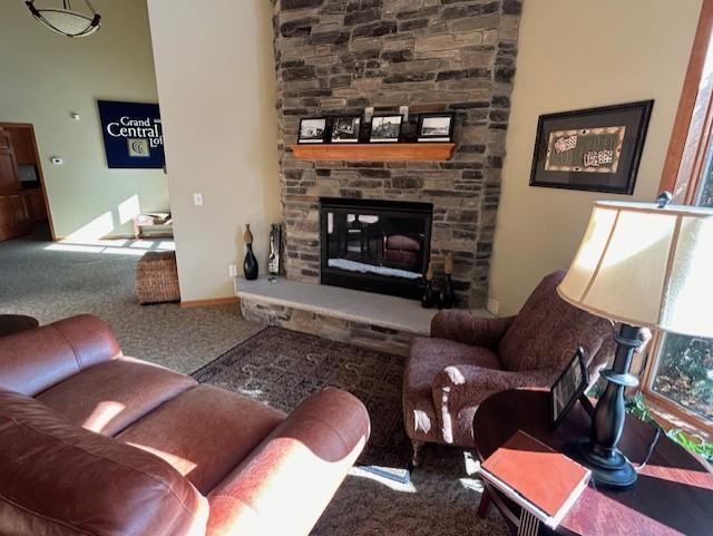 carpeted living room featuring a stone fireplace and baseboards
