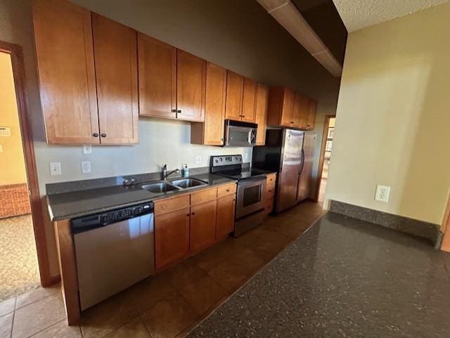 kitchen with baseboards, a textured ceiling, brown cabinetry, stainless steel appliances, and a sink