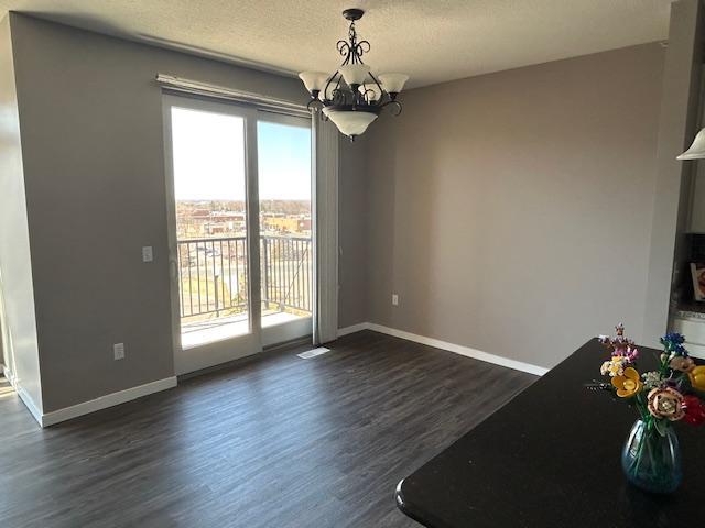 unfurnished dining area featuring a notable chandelier, a textured ceiling, baseboards, and dark wood-style floors