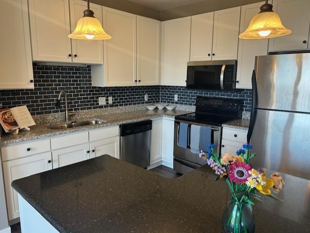 kitchen with white cabinetry, dark stone countertops, a sink, stainless steel appliances, and backsplash