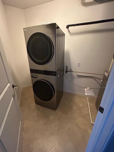 clothes washing area with baseboards, stacked washer and dryer, and laundry area