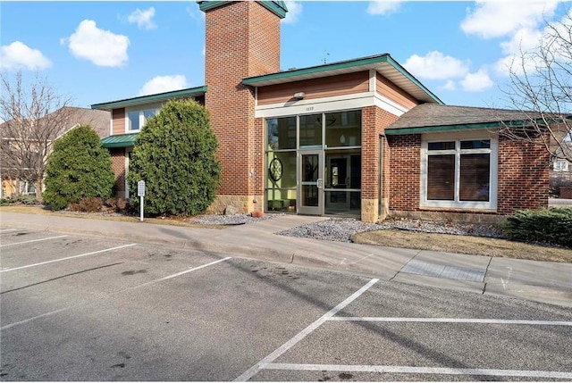 exterior space with uncovered parking, a chimney, and brick siding