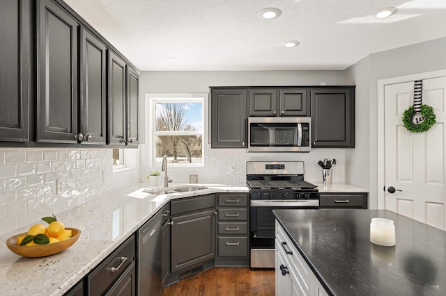 kitchen with decorative backsplash, dark wood-style flooring, appliances with stainless steel finishes, light stone countertops, and a sink
