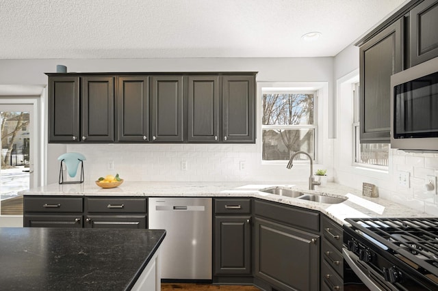 kitchen with a textured ceiling, tasteful backsplash, a sink, light stone counters, and stainless steel appliances