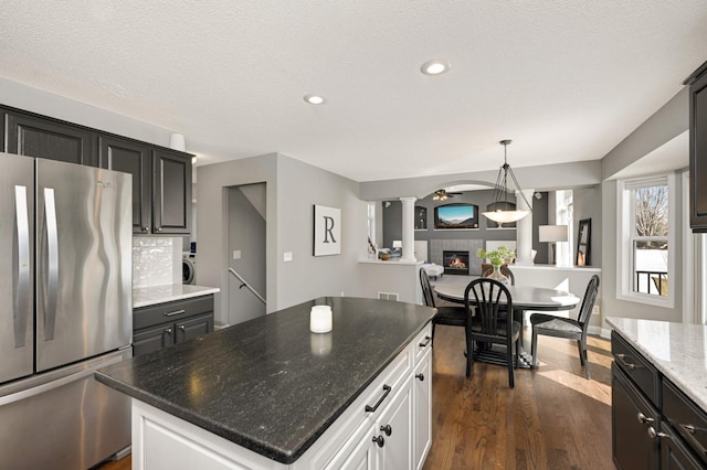 kitchen with freestanding refrigerator, a center island, dark stone counters, a tiled fireplace, and dark wood finished floors