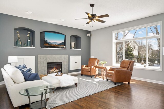 living area featuring a ceiling fan, baseboards, wood finished floors, and a fireplace