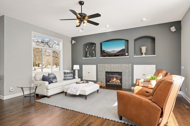 living room with baseboards, a fireplace, a ceiling fan, and dark wood-style floors