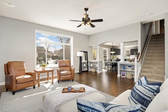 living area featuring ornate columns, stairs, ceiling fan, and wood finished floors