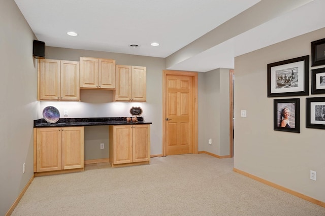 kitchen with light brown cabinets, baseboards, light carpet, and built in desk