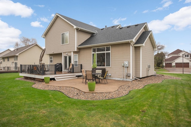 rear view of house with roof with shingles, a wooden deck, a lawn, and a patio area