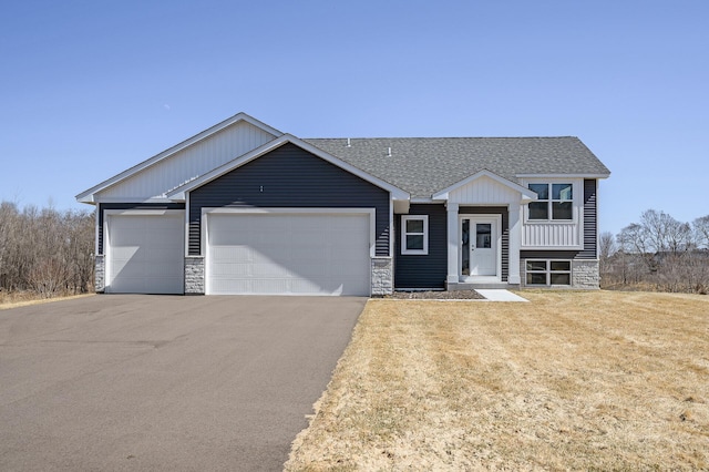 view of front of property featuring driveway, stone siding, an attached garage, a front lawn, and a shingled roof