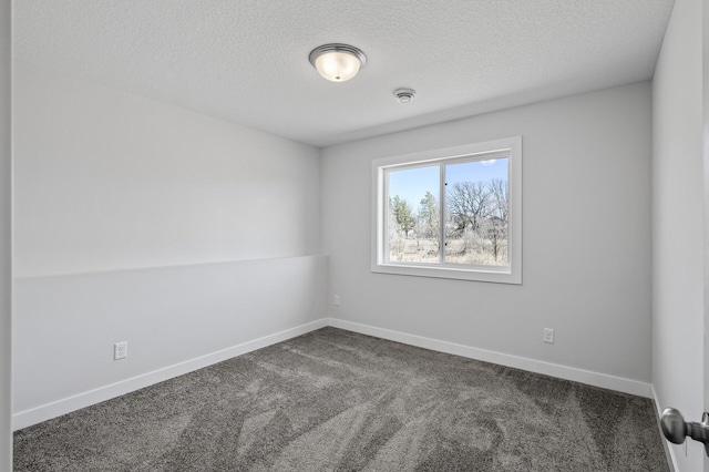 empty room with a textured ceiling, dark colored carpet, and baseboards