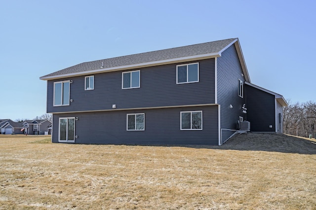 rear view of house featuring central AC unit and a lawn