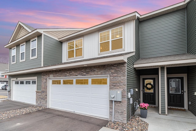townhome / multi-family property featuring stone siding, aphalt driveway, and a garage