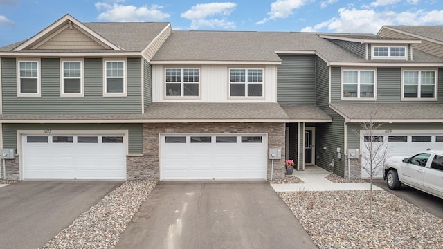 townhome / multi-family property with driveway, a shingled roof, and an attached garage