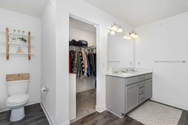 full bathroom with baseboards, wood finished floors, toilet, vanity, and a walk in closet