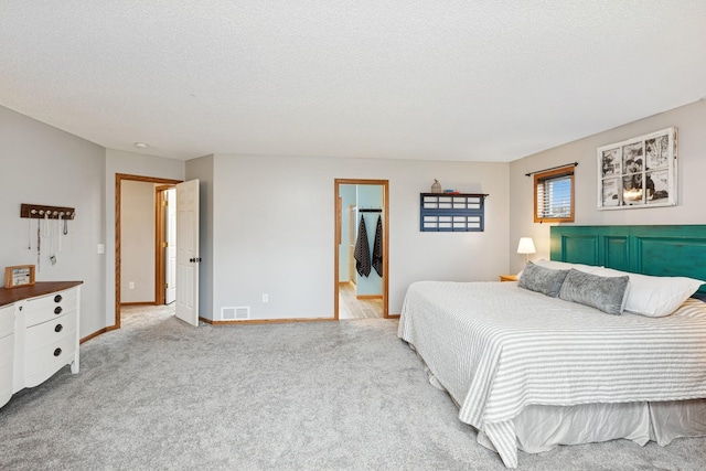 bedroom with visible vents, a textured ceiling, baseboards, and light carpet