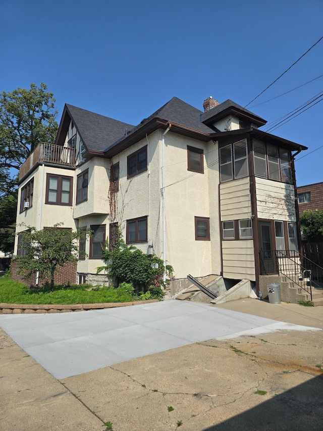 view of front of property featuring a chimney, a balcony, and stucco siding