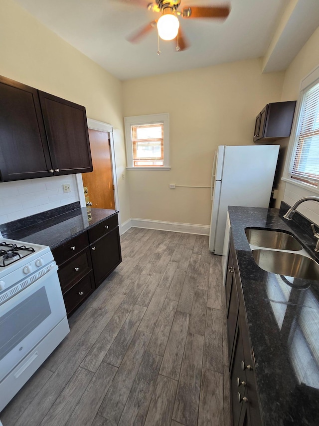 kitchen featuring dark stone countertops, gas range, a sink, ceiling fan, and wood finished floors