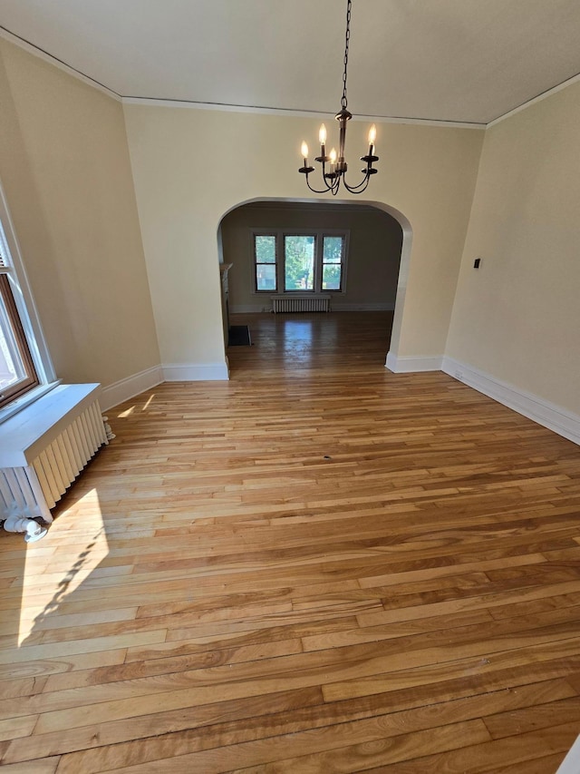 unfurnished dining area with arched walkways, radiator, an inviting chandelier, and light wood-type flooring
