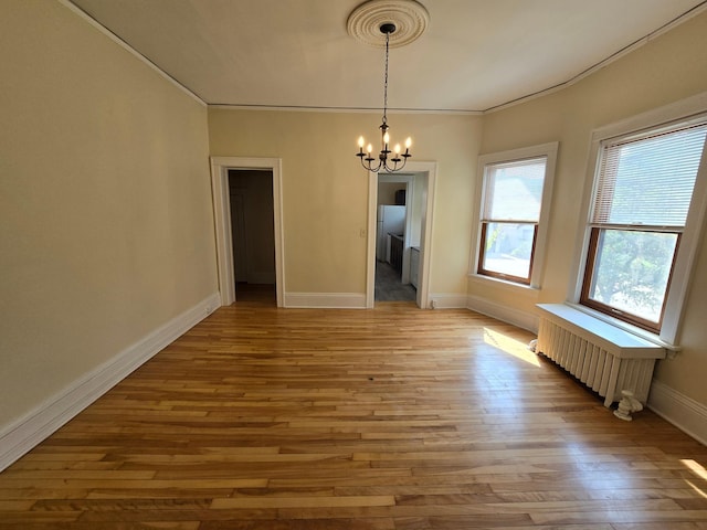 unfurnished dining area with radiator heating unit, ornamental molding, a chandelier, wood finished floors, and baseboards