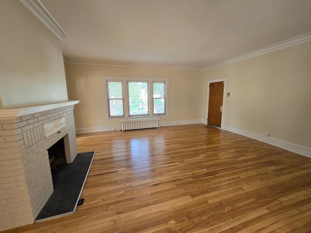 unfurnished living room with baseboards, a brick fireplace, ornamental molding, radiator, and light wood-style flooring